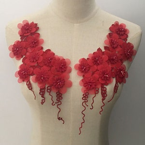Könnte beinhalten: Rote Blumenapplikation mit Perlenakzenten und herabhängenden Strängen. Diese zarte Verzierung ist perfekt, um Kleidung, Accessoires oder Heimdekorprojekten einen Hauch von Eleganz zu verleihen.
