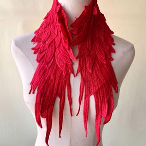 May include: A red fabric collar with a feather-like design. The collar is made of a soft, textured fabric and has a delicate, flowing shape.