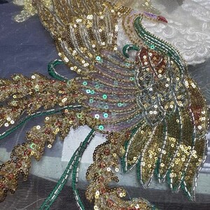 May include: A gold and green beaded peacock design on a sheer fabric. The peacock is detailed with sequins and beads.