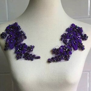 Pode incluir: Dois apliques florais de contas roxas com lantejoulas iridescentes sobre um fundo branco.
