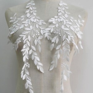 May include: White lace applique with a delicate floral design featuring leaves and small white flowers. This applique is perfect for adding a touch of elegance to wedding dresses, bridal accessories, or other craft projects.