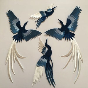 May include: Four blue and white embroidered bird appliques with long tails. The birds are in various poses with their wings spread.