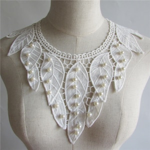 Könnte beinhalten: Weißer Spitzenkragen mit Blattdesign und Perlenbesatz.