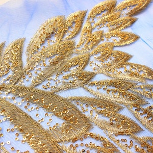 May include: Gold leaf embroidery trim with sequins on a light blue mesh fabric. The trim features a repeating pattern of stylised leaves.