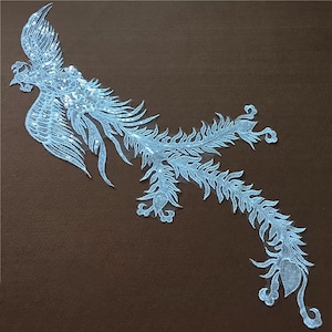 Peut inclure: Une applique brodée bleu clair représentant un phénix avec une longue queue. Le phénix est un oiseau mythique qui symbolise la renaissance et l'immortalité.