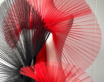 May include: A garment accessory featuring large, pleated, fan-like structures made of sheer red and black tulle fabric. The design consists of layered, semi-transparent mesh panels that radiate outward, creating a voluminous, sculptural appearance.