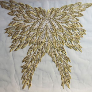 May include: Gold embroidered applique with a feather design. The applique is made of a sheer fabric with gold thread and sequins.