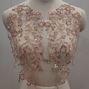 Peut inclure: Une applique de perles et de paillettes dorées roses avec un motif floral. L'applique est parfaite pour ajouter une touche d'éclat à n'importe quel vêtement.