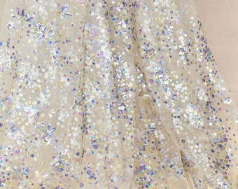 May include: A sheer beige fabric with iridescent sequins and stars in shades of blue, purple, and gold.