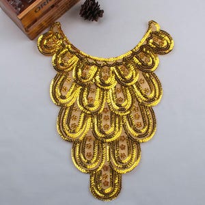 May include: Gold sequined neckline trim with a scalloped design. The trim is made of sequins and beads and is perfect for adding a touch of glamour to any garment.