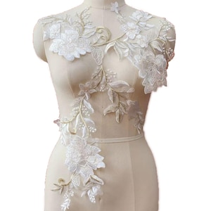 Może przedstawiać: Biała aplikacja z koronki kwiatowej z delikatnymi koralikami i wzorem winorośli. Koronka idealnie nadaje się do dodania odrobiny elegancji do każdego ubrania lub projektu.