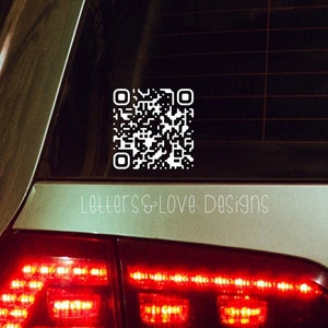 May include: A white QR code sticker on the back window of a silver car. The sticker is on the lower right side of the window and says "Letters & Love Designs" below it.