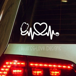May include: White vinyl decal of a stethoscope, heart, and heartbeat line on a car window. The decal says "Letters & Love Designs" at the bottom.