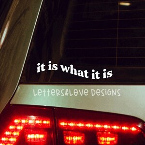May include: A silver car with a white vinyl sticker on the back window that reads "it is what it is" and "letters&love designs".