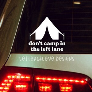 May include: A white car with a white vinyl sticker on the back window. The sticker features a white tent graphic and the text "don't camp in the left lane" with the text "letters&love designs" below.