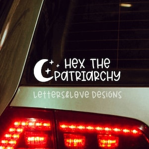 May include: A white vinyl sticker on the back window of a car. The sticker features a crescent moon and stars with the text "Hex the Patriarchy". The text "Letters & Love Designs" is also included on the sticker.