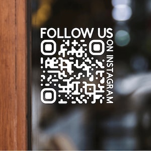 May include: White text on a glass surface reads "FOLLOW US" above a QR code, with "ON INSTAGRAM" written vertically to the right. The background is blurred, with a wooden door frame on the left.