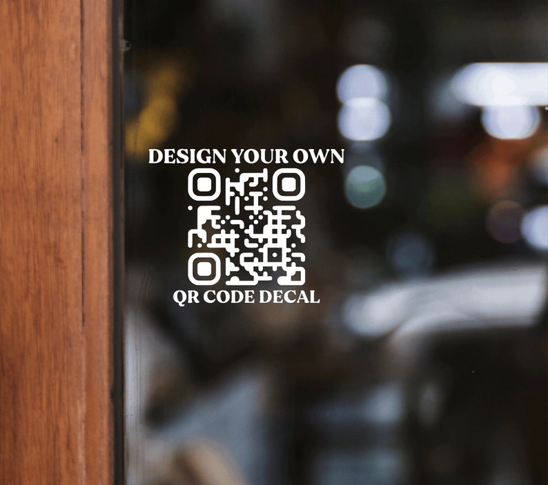 A mockup of what this QR code vinyl decal from Letters And Love Designs would look like on the front door of a shop. On the top of the QR code it says, design your own and below the QR it says, QR code Decal. You would customize the exact wording.