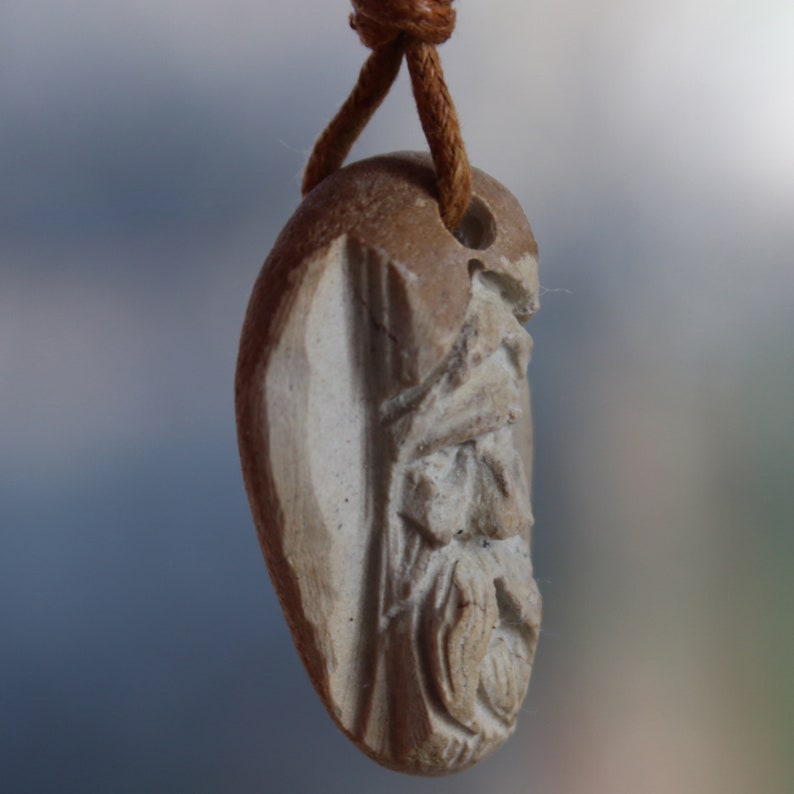 May include: A brown and white stone pendant with a carved face, hanging from a brown leather cord.