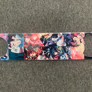 May include: A metal bottle opener with a colorful anime design featuring multiple characters. The characters are in a variety of poses and expressions, with a red, blue, and white color scheme.