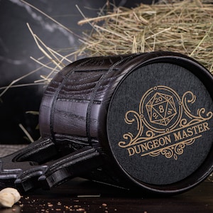 May include: A black wooden mug with a handle and a black and gold design. The design features a 20-sided die and the text "Dungeon Master".