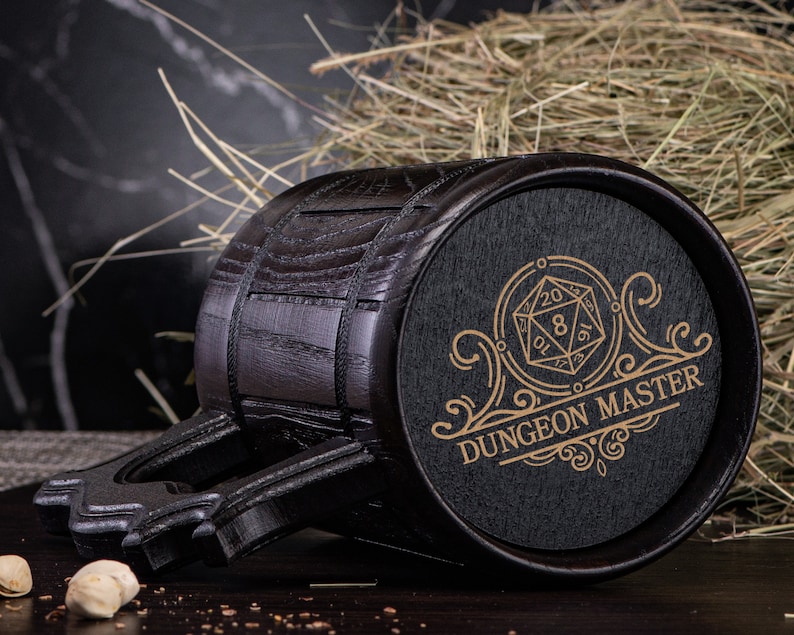 May include: A black wooden mug with a handle and a black and gold design. The design features a 20-sided die and the text "Dungeon Master".
