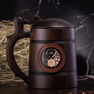 May include: A dark brown wooden beer stein with a lid and a large handle. The stein features a circular leather patch with a die design. The handle has a unique, decorative shape. The stein is designed for beverages.
