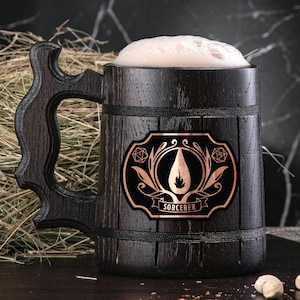 May include: A dark brown wooden beer stein with a black and gold design. The stein has a handle and a label that says "Sorcerer".