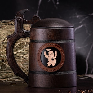May include: A dark brown wooden beer stein with a matching lid and handle. The stein features a circular leather patch with a carved figure. The handle has a unique, decorative design. The stein is a classic, rustic style.