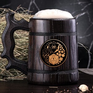 May include: A dark wooden beer stein filled with beer and foam. The stein has a decorative handle and a gold emblem with dice numbers. The background includes hay and a dark marble surface.