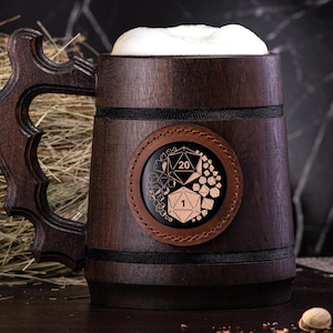 Puede incluir: Una jarra de cerveza de madera de color marrón oscuro con un asa grande y ornamentada y un parche circular de cuero en la parte delantera. El parche presenta un diseño gráfico en blanco y negro de dados poliédricos, incluyendo un dado de 20 caras.
