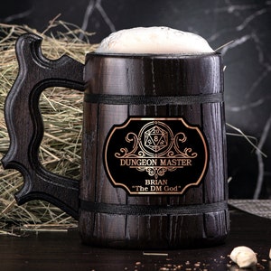 May include: A dark brown wooden beer stein with a black leather strap and a metal plaque that reads "Dungeon Master Brian "The DM God"". The stein is filled with a light brown liquid and has a white foam head.