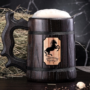 May include: A dark brown wooden beer stein with a black handle. The stein has a black band around the top and a wooden plaque with a black silhouette of a horse and the text "The Prancing Pony".