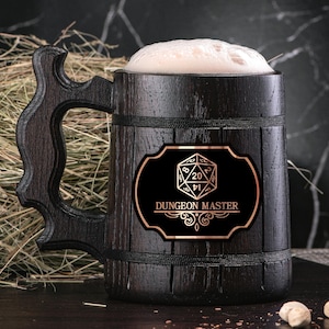 May include: A dark brown wooden beer stein with a black and gold label that says "Dungeon Master" and features a 20-sided die. The stein is filled with a light-colored beverage.