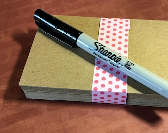 May include: A stack of brown kraft paper note cards with a pink polka dot ribbon and a black Sharpie permanent marker with a fine point.