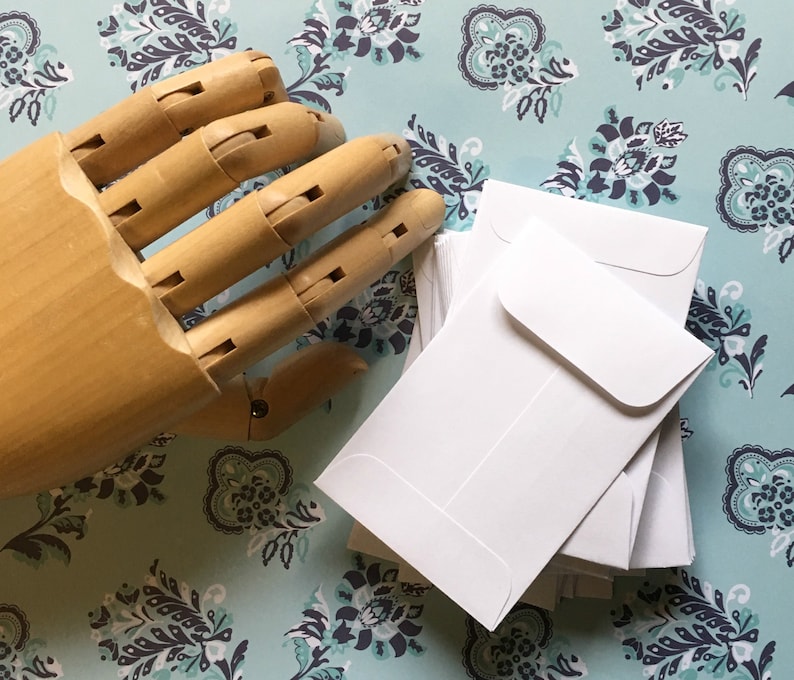 May include: A stack of white envelopes with rounded corners on a patterned background. The envelopes are blank and have a flap on the top.