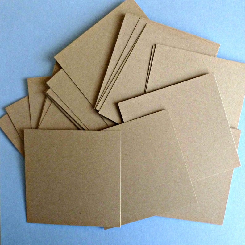May include: A stack of brown cardstock paper squares. The paper is a light brown color and has a slightly textured surface.