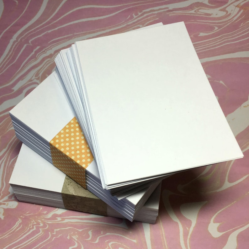 Puede incluir: Una pila de tarjetas blancas en blanco con una cinta de lunares amarillos y blancos envuelta alrededor de la parte inferior de la pila.