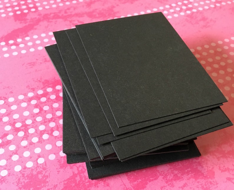 Pu&ograve; includere: Una pila di carte rettangolari nere. Le carte sono disposte ordinatamente, con i bordi allineati, creando un aspetto uniforme. Lo sfondo &egrave; una superficie rosa con pois bianchi.