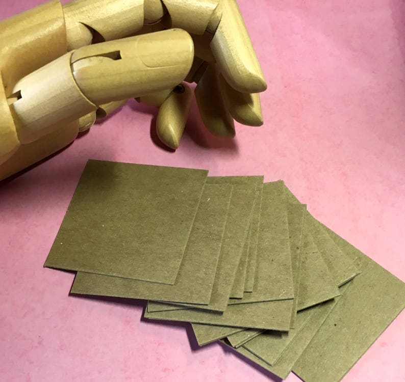 May include: A stack of brown square paper cards, with a wooden hand model in the background.