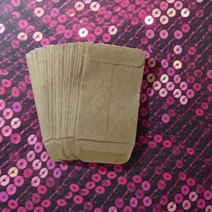 May include: A stack of brown paper envelopes, with a flap on the top, against a pink and black sequin background.