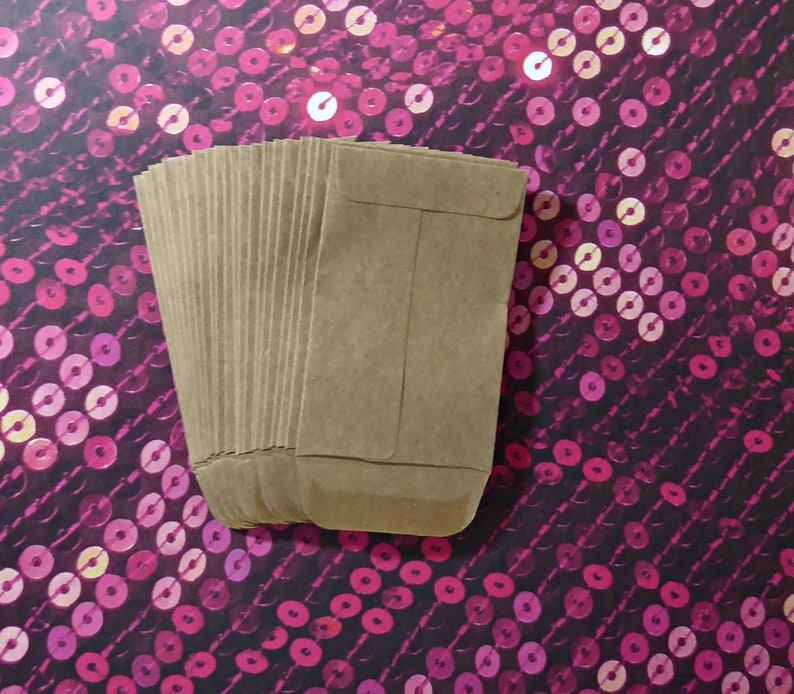 May include: A stack of brown paper envelopes, with a flap on the top, against a pink and black sequin background.