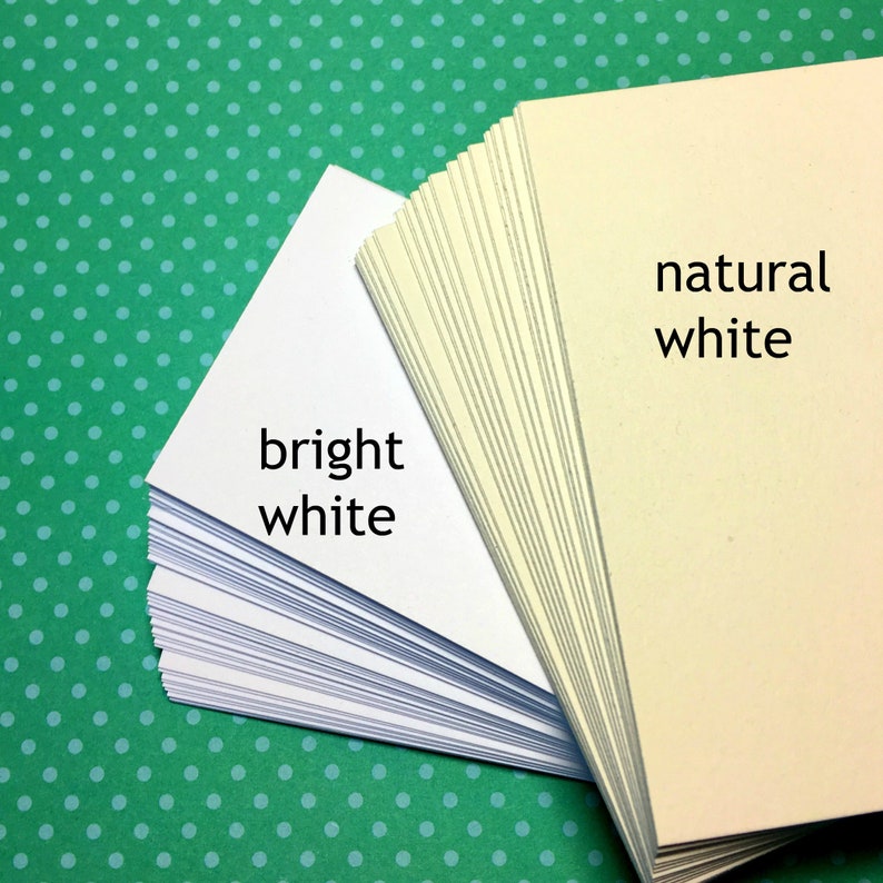 Puede incluir: Dos pilas de papel, una blanca brillante y otra blanca natural. El texto "bright white" est&aacute; escrito en la pila de la izquierda y "natural white" est&aacute; escrito en la pila de la derecha.