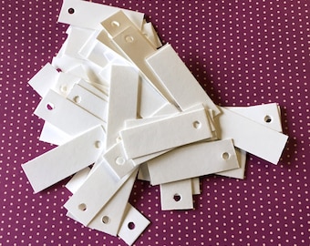May include: A pile of white rectangular paper tags with a hole punched in the top. The tags are on a pink and white polka dot background.