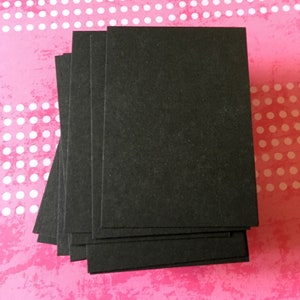 Pu&ograve; includere: Una pila di carte nere rettangolari, forse per l'artigianato o per prendere appunti, &egrave; disposta su uno sfondo rosa con pois bianchi. Le carte sono realizzate in un materiale scuro e opaco.