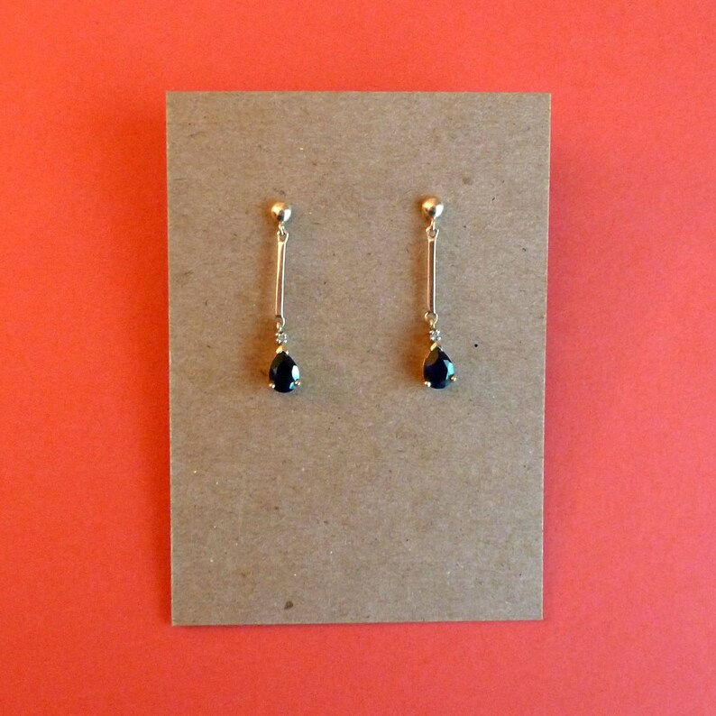 May include: A pair of gold earrings with black teardrop-shaped stones hanging from thin gold bars.
