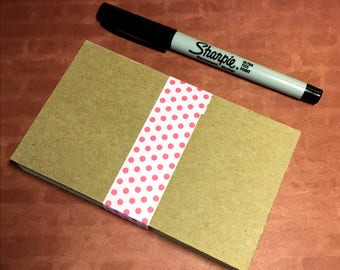 May include: A stack of brown note cards with a pink polka dot ribbon tied around them. A black Sharpie Ultra Fine Point permanent marker is lying on a brown surface.
