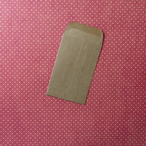 May include: A brown paper envelope with a flap on the top. The envelope is lying on a red background with white polka dots.