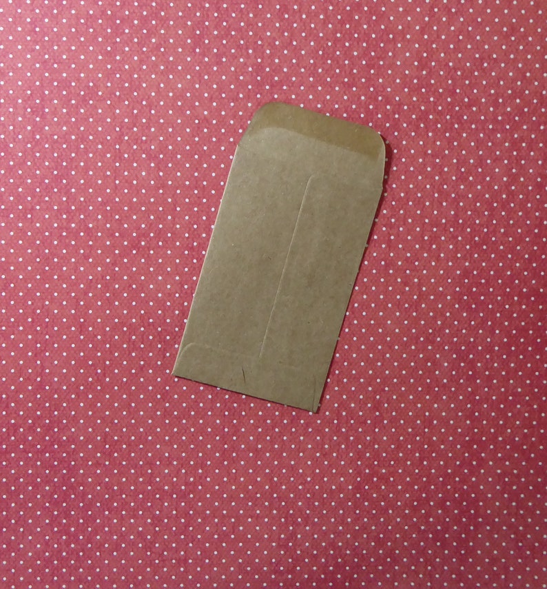 May include: A brown paper envelope with a flap on the top. The envelope is lying on a red background with white polka dots.