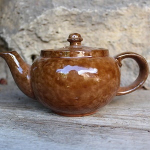 Könnte beinhalten: Eine braune Teekanne aus Keramik mit rundem Korpus und Deckel. Die Teekanne hat einen Ausguss und einen Henkel.